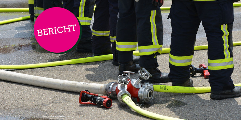 KI generiert: Das Bild zeigt Feuerwehrleute in Einsatzkleidung, die um Schläuche und Verteiler auf der Straße stehen. Im Vordergrund ist ein runder, pinker Kreis mit dem Wort "BERICHT" zu sehen.