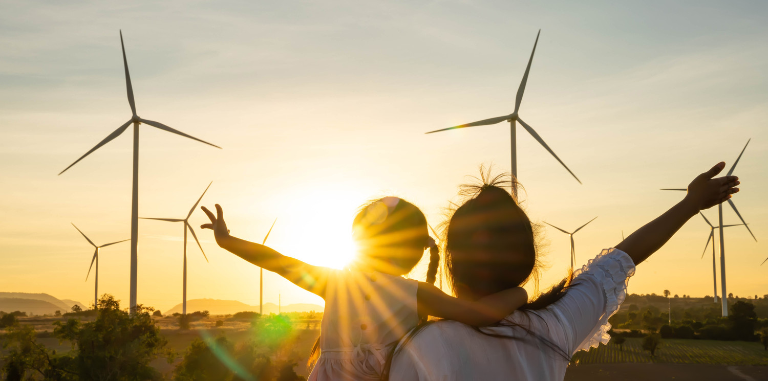 KI generiert: Das Bild zeigt eine erwachsene Person und ein Kind, die bei Sonnenuntergang vor mehreren Windkraftanlagen stehen und ihre Arme ausstrecken. Der Hauptinhalt des Bildes ist die Verbindung von Mensch und erneuerbarer Energie, symbolisiert durch die Windräder im Hintergrund.