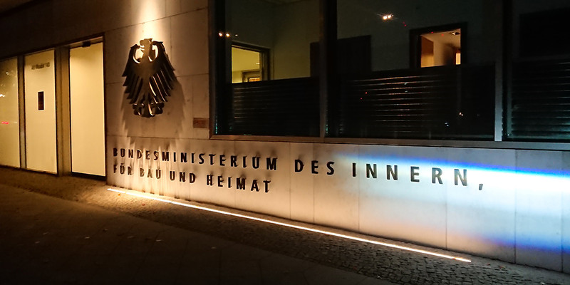KI generiert: Das Bild zeigt den Eingang des Bundesministeriums des Innern, für Bau und Heimat in Deutschland. Der Schwerpunkt liegt auf der Gebäudeaufschrift und dem Bundesadler-Emblem neben dem Eingang.