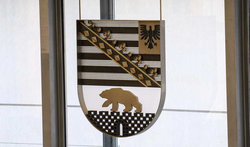 KI generiert: Das Bild zeigt ein Wappen mit einem schwarzen Adler auf goldenem Grund in der oberen Hälfte und einem goldenen Bären auf schwarzem Grund in der unteren Hälfte. Der Hauptinhalt des Bildes ist das Wappen, das zwischen zwei Fenstern hängt.